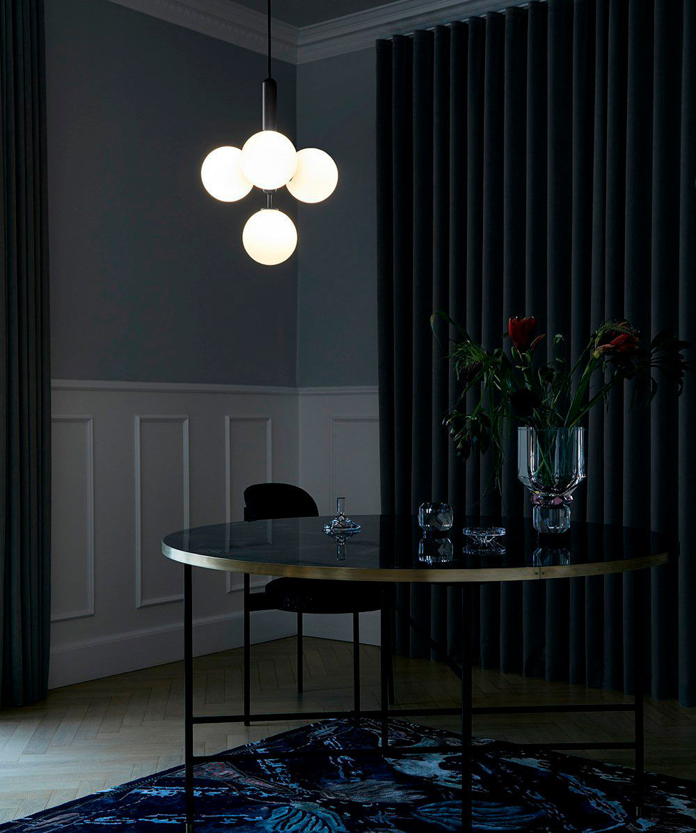 Four opal globes glow on a black-rod Clérachic pendant above a dark round table, with navy curtains behind.