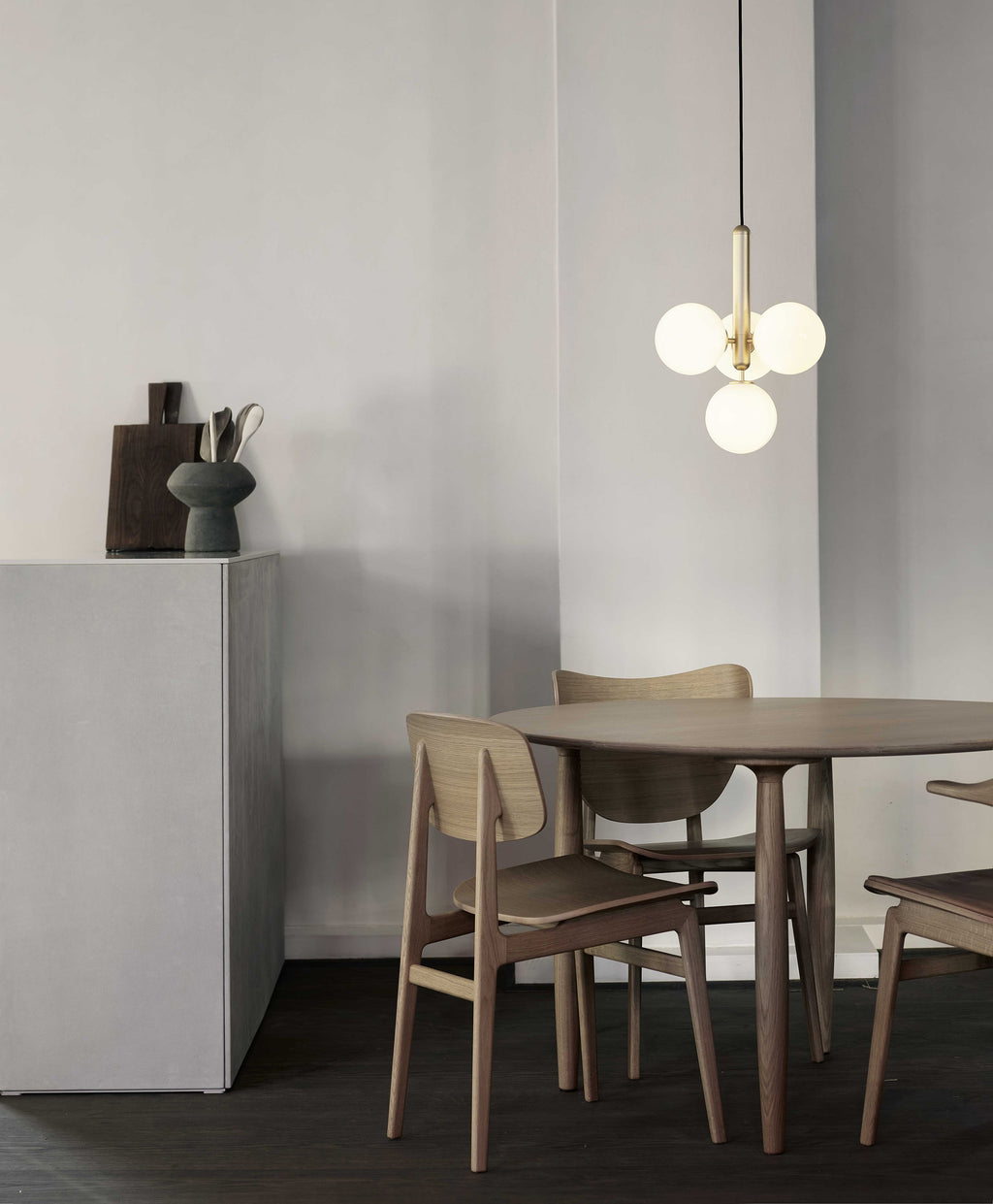 Brass-rod Clérachic pendant with four white globes hangs above a round wooden table and light wood chairs.