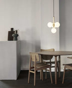 Brass-rod Clérachic pendant with four white globes hangs above a round wooden table and light wood chairs.