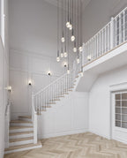 A cascade of Clérachic pendants with clear and opal globes hangs through a white stairwell with a wooden banister.