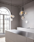 Two black-rod Clérachic cluster pendants with clear textured globes hang in a tall room with an arched window.