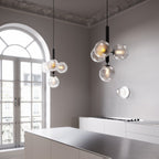 Close-up angle of two Clérachic cluster pendants with textured clear globes, a black rod and arched window behind.