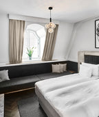 A Clérachic cluster pendant with four white globes hangs over a bed in a room with arched window and grey curtains.