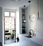 Three single-globe Clérachic pendants on black rods hang over a kitchen counter with a herringbone tile wall.