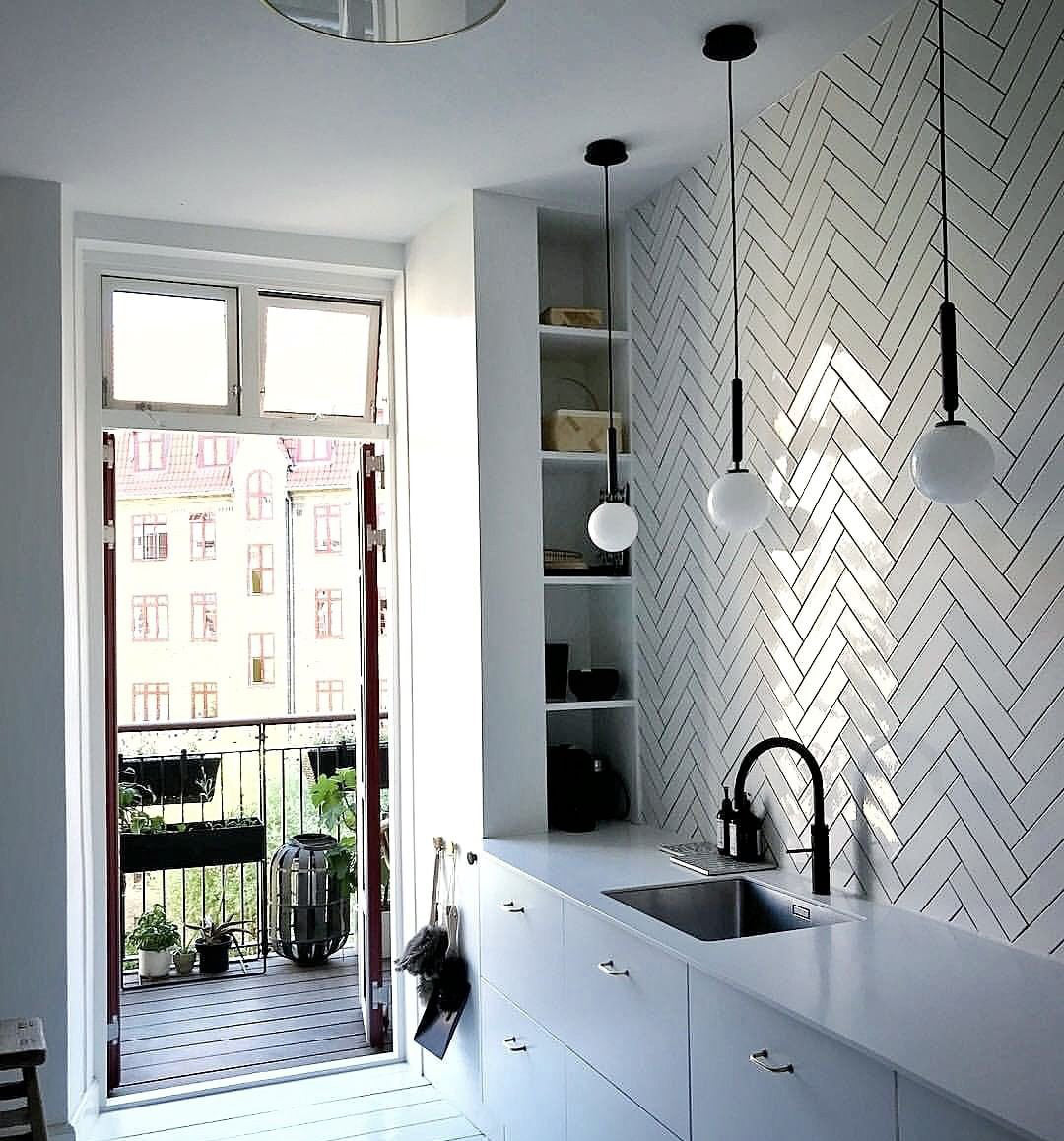 Three single-globe Clérachic pendants on black rods hang over a kitchen counter with a herringbone tile wall.