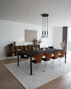 Black-rod Clérachic pendant with white globes hangs on a round ceiling plate over a black dining table and rug.