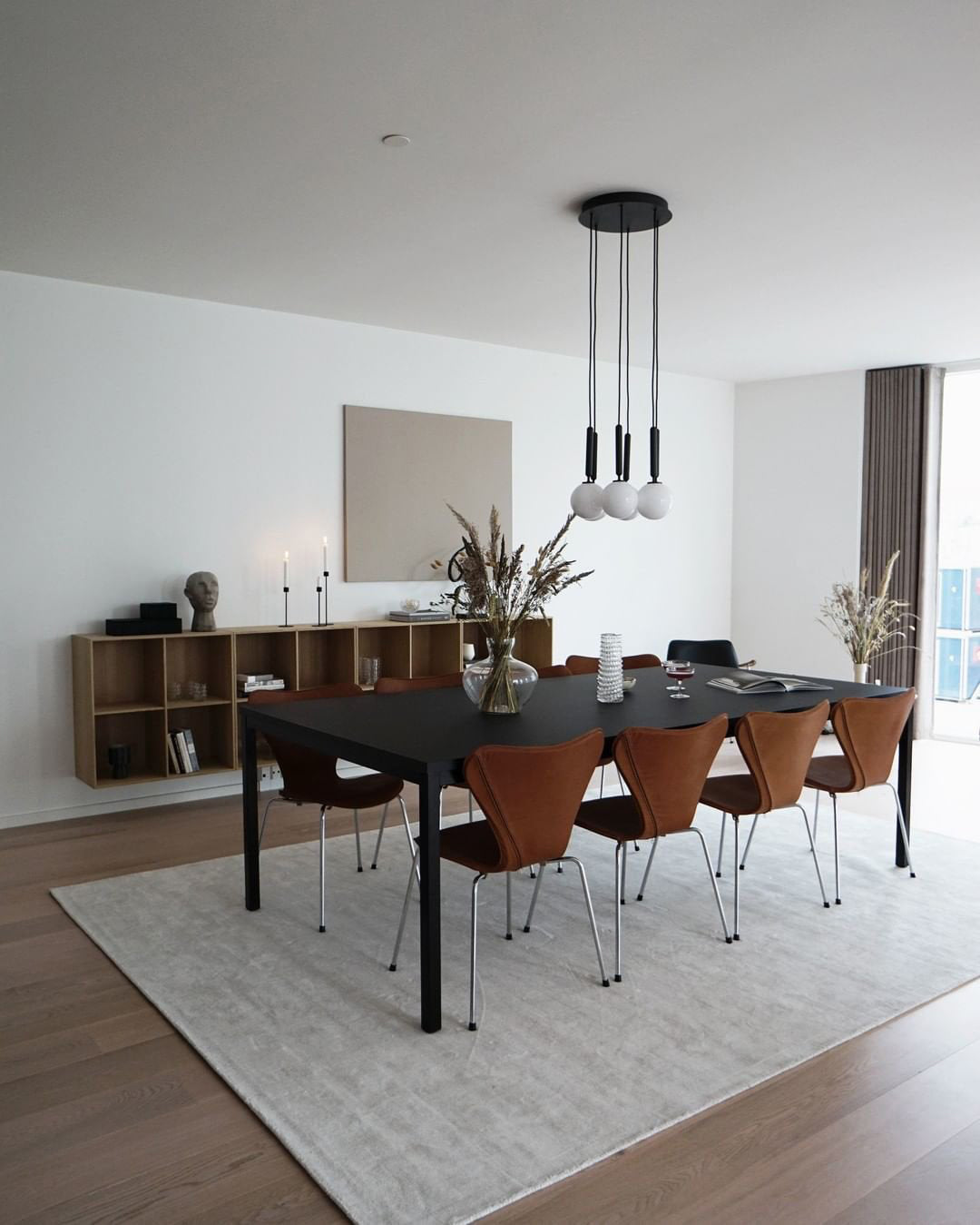 Black-rod Clérachic pendant with white globes hangs on a round ceiling plate over a black dining table and rug.