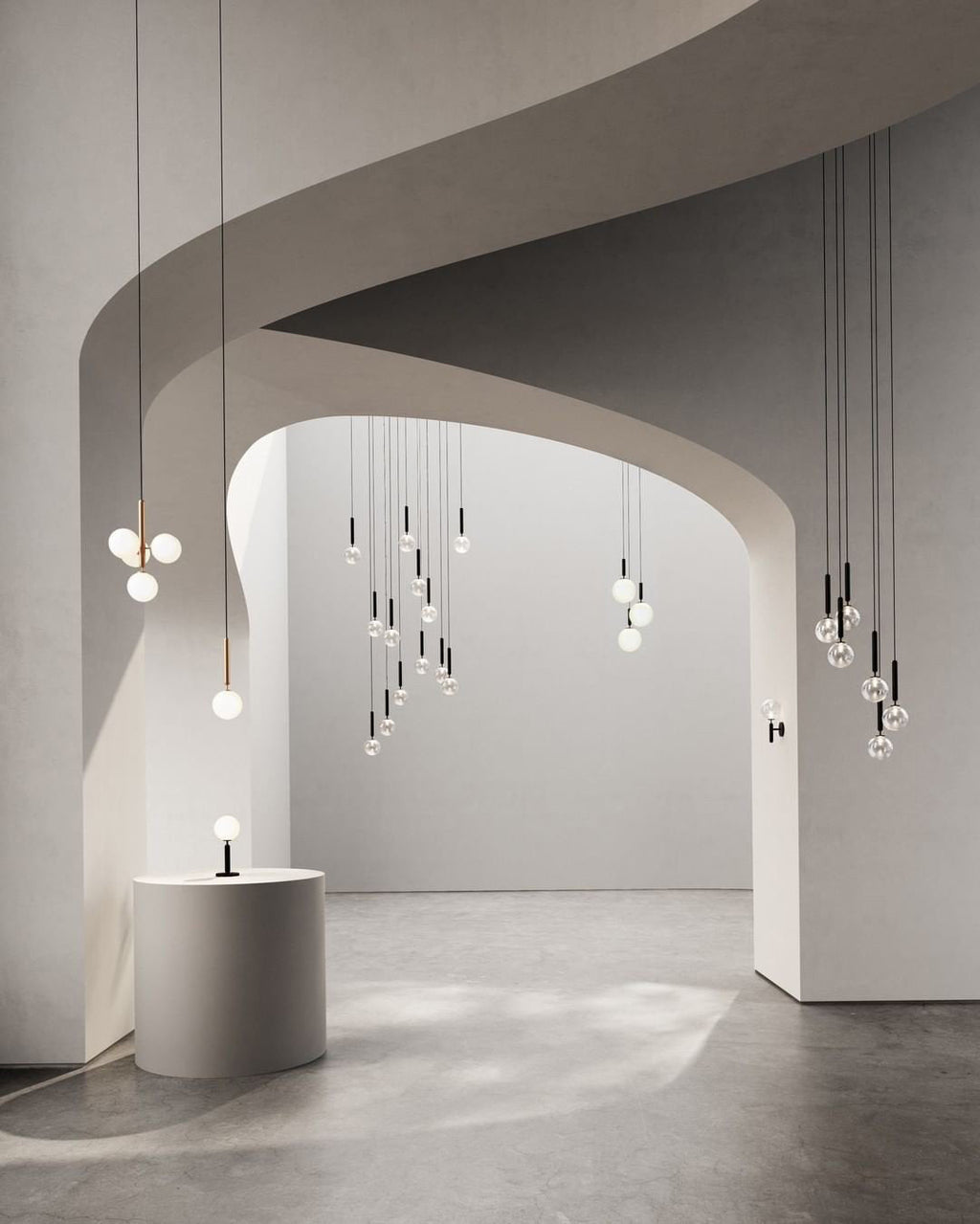 Tall stair-height drop of Clérachic pendants with white globes beside a curved wall, plus lamps on a stone plinth.