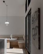 Black-rod Clérachic pendant with a small white-globe cluster hangs on a swagged cord in a bright, open room.