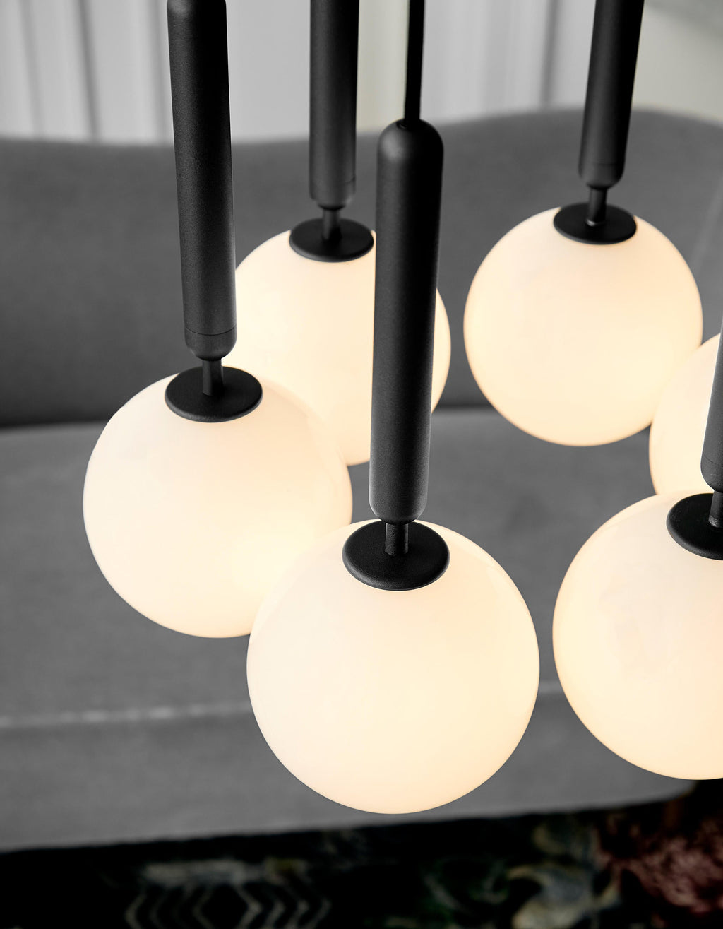 Close view of white opal globes and black rods on this Clérachic pendant, glowing warm over a grey sofa.