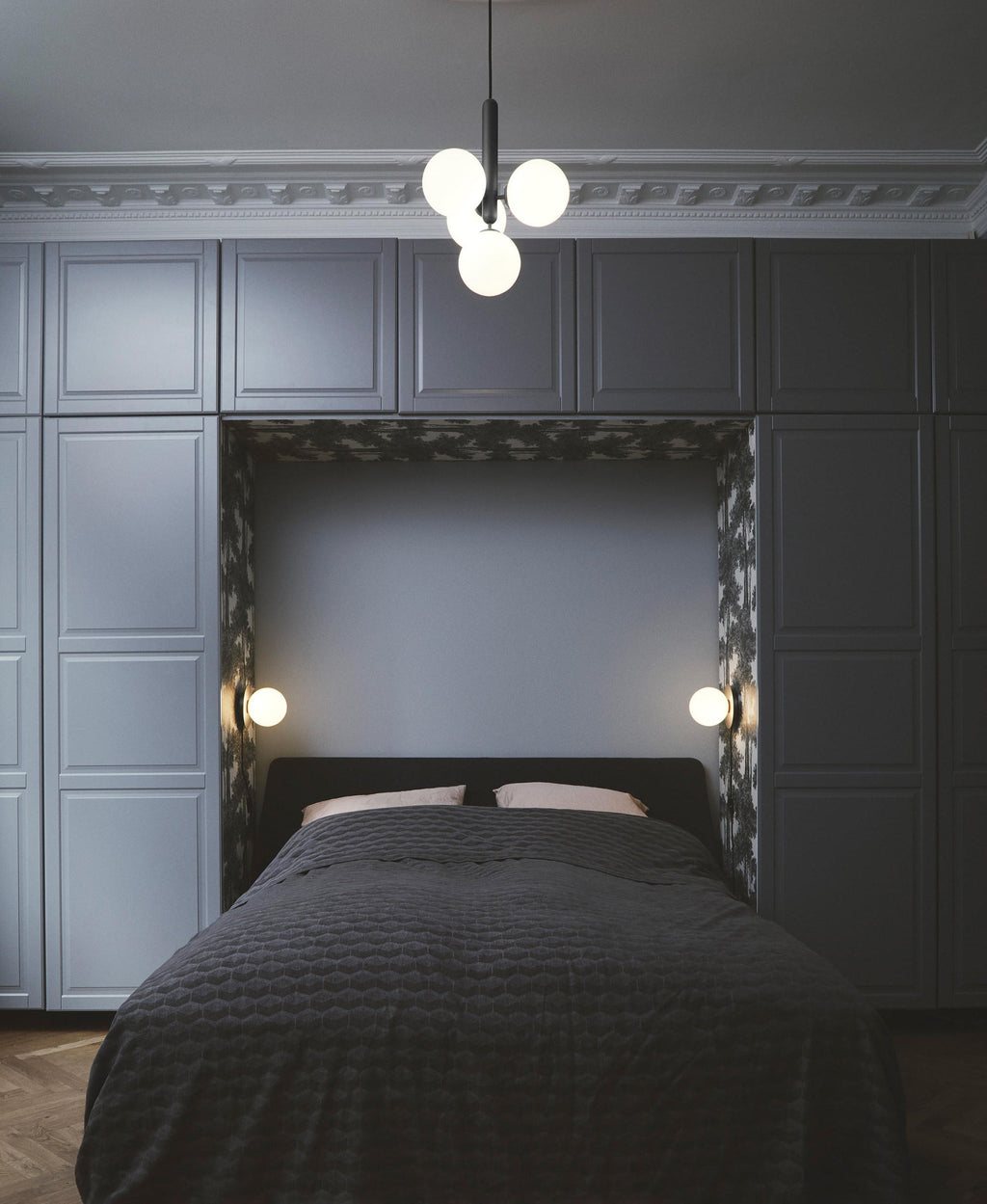 Four-globe Clérachic pendant with white opal glass hangs above a bed in a dark panelled room.