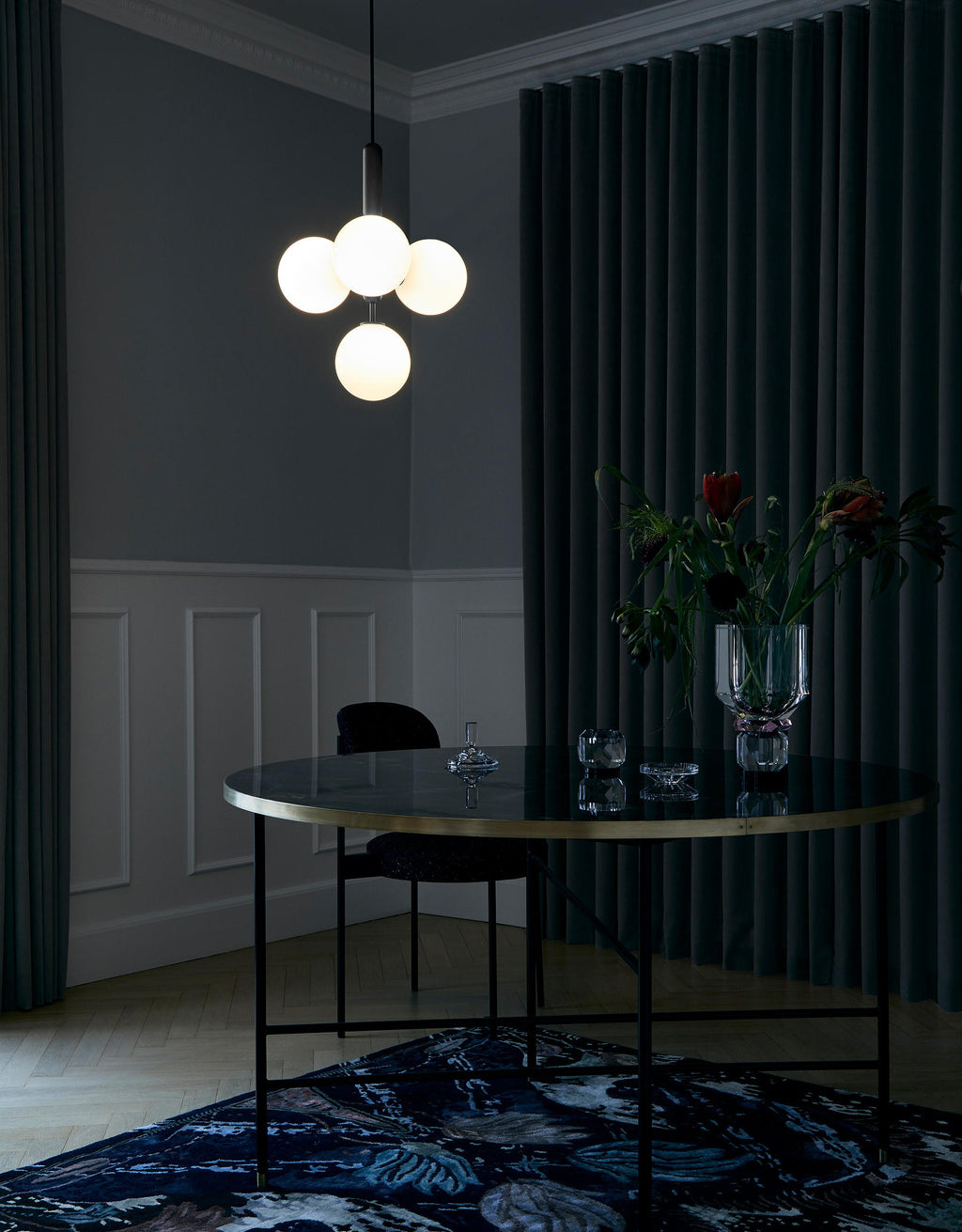 A Clérachic cluster pendant with white globes lit warm above a dark round table in a deep green room.
