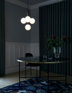 A Clérachic cluster pendant with white globes lit warm above a dark round table in a deep green room.