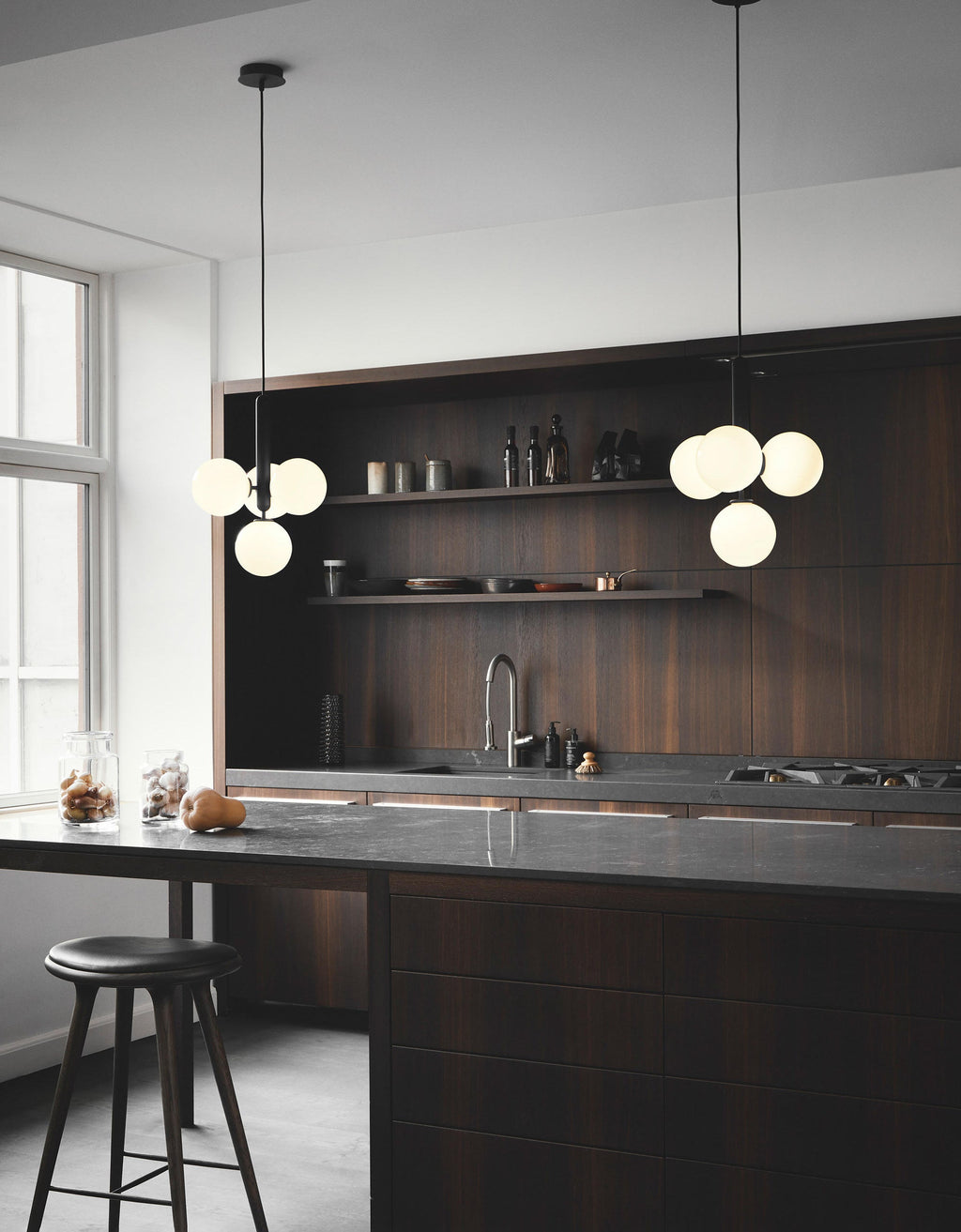 Two Clérachic cluster pendants with white opal globes hang over a dark wood kitchen island with a bar stool.