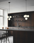 Two Clérachic cluster pendants with white opal globes hang over a dark wood kitchen island with a bar stool.