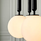 Close view of two lit opal globes and their black rods on this Clérachic pendant against a pale panelled wall.