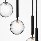 Close view of clear textured glass globes with visible filaments on black rods from this Clérachic pendant.