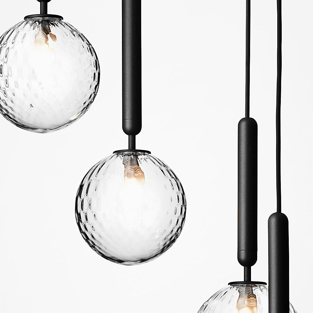 Close view of clear textured glass globes with visible filaments on black rods from this Clérachic pendant.