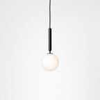 Single Clérachic pendant with a black rod and one white opal globe, lit softly against a pale grey backdrop.