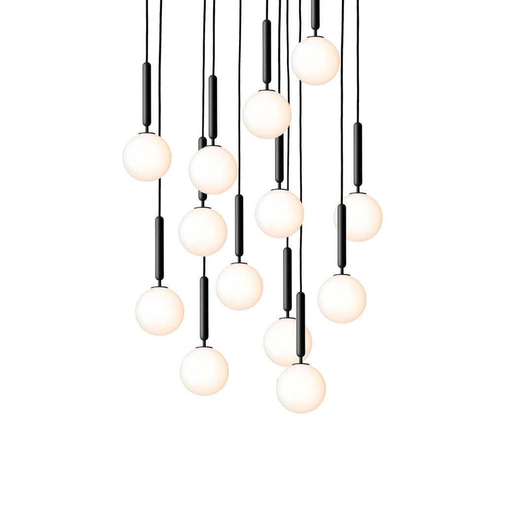 Clérachic pendants with white opal globes on black rods hang in a long cascade, lit warm on a white background.