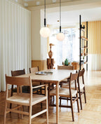 Two Clérachic pendants with white opal globes hang at different heights over a pale oak table and chairs.
