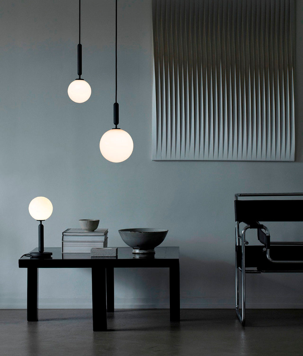 Two Clérachic pendants with white globes hang at different heights above a low black table in a blue-grey room.