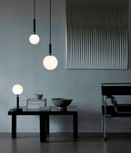 Two Clérachic pendants with white globes hang at different heights above a low black table in a blue-grey room.
