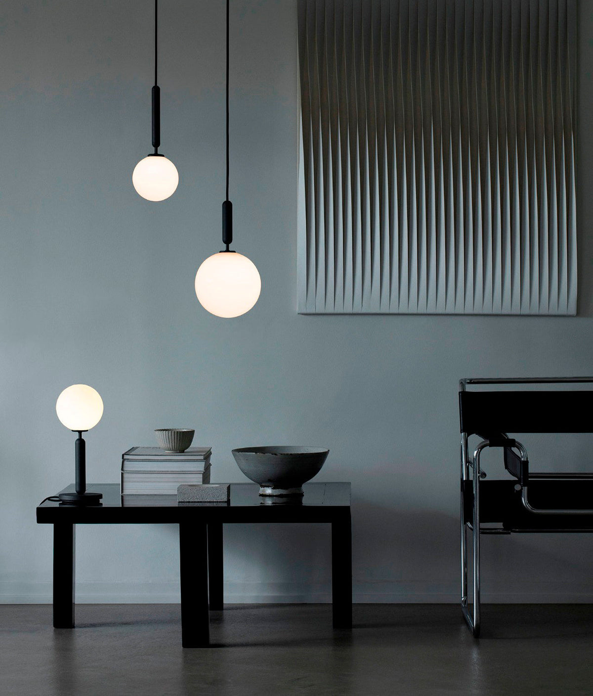 Two Clérachic pendants with white globes hang at different heights above a low black table in a blue-grey room.