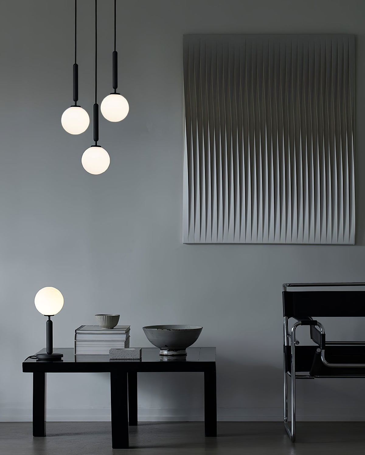 Three black-rod Clérachic pendants with opal globes hang at different heights above a low table and wall panel.