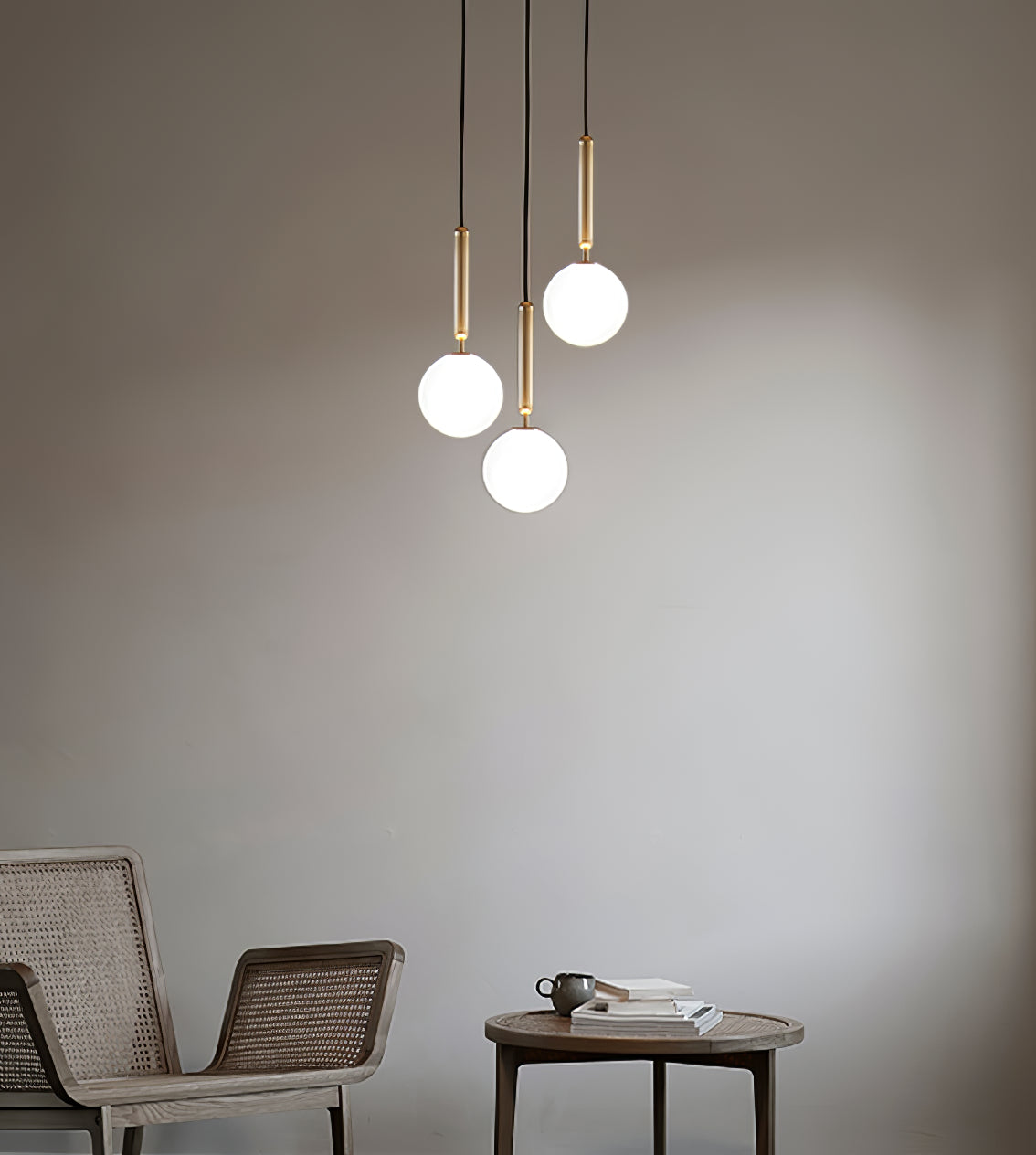 Three brass-rod Clérachic pendants with white globes hang in a loose group in front of a warm grey wall.