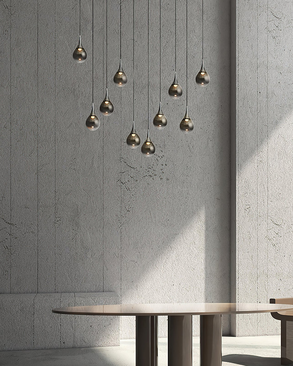 Smoked-glass Clérachic pendants hang at staggered heights against a rough grey concrete wall, above a round table.