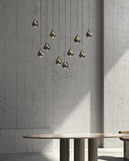 Smoked-glass Clérachic pendants hang at staggered heights against a rough grey concrete wall, above a round table.
