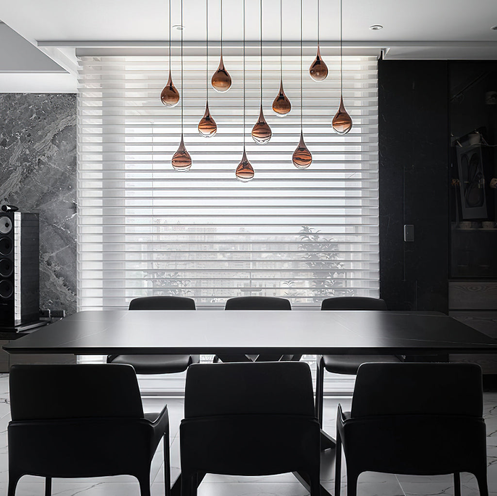 Rose gold Clérachic pendants hang in a staggered group in front of a blinds-covered window, above a black dining table.