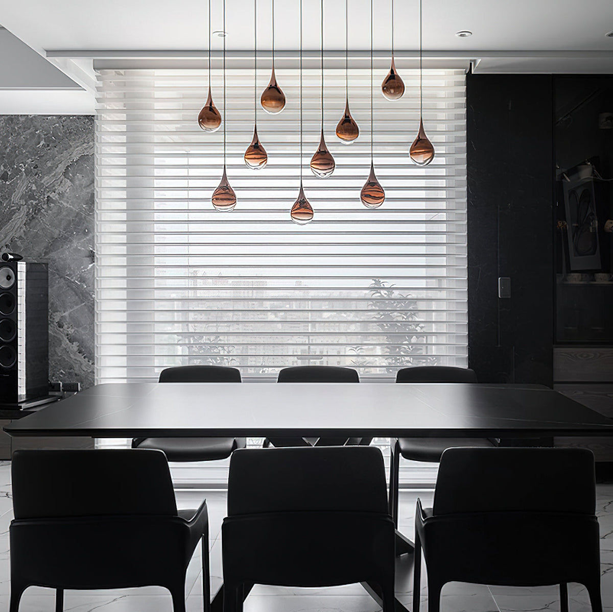 Rose gold Clérachic pendants hang in a staggered group in front of a blinds-covered window, above a black dining table.
