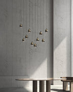 A tall grouped drop of smoke-toned Clérachic pendants in front of a concrete wall, above a low round table.