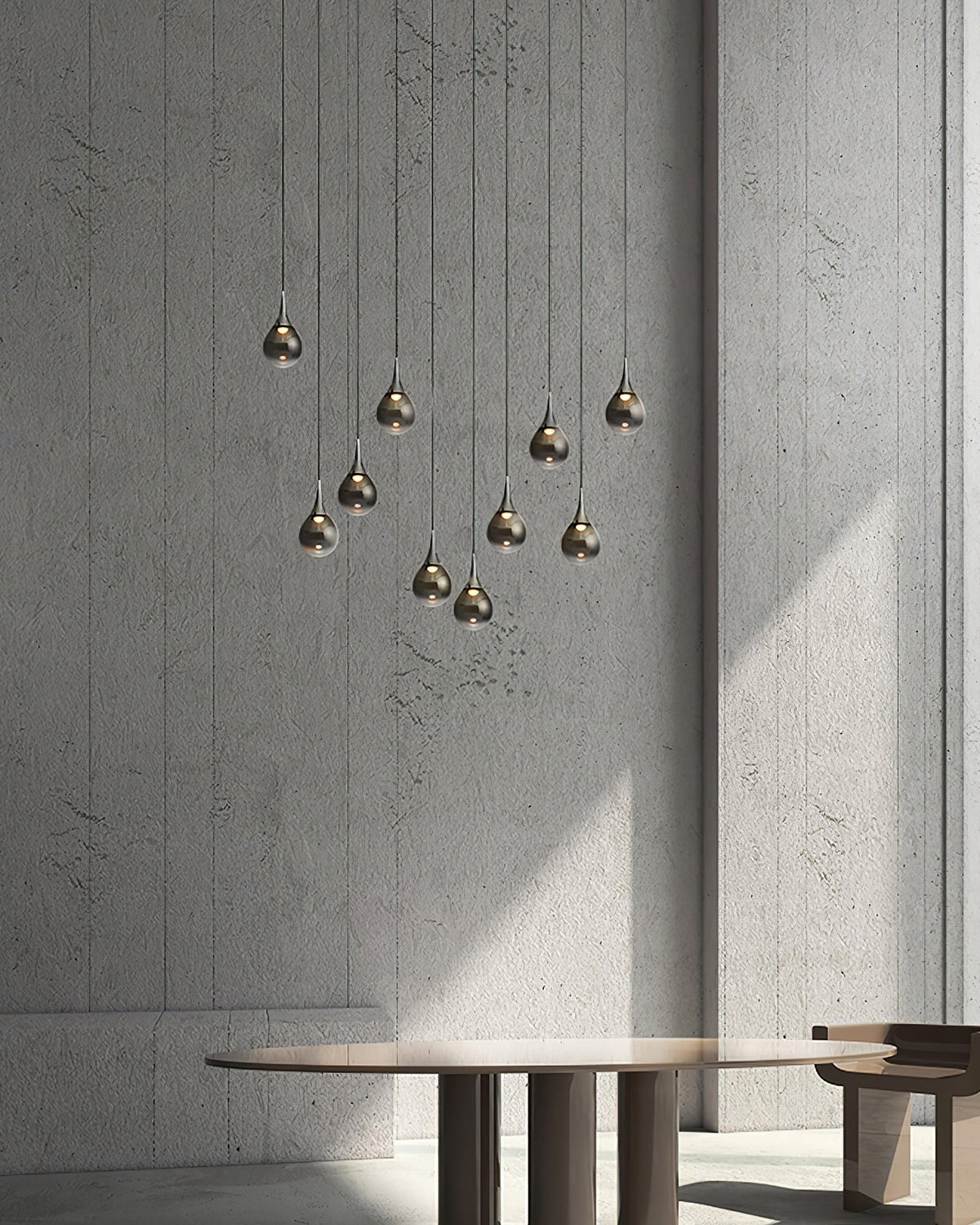 A tall grouped drop of smoke-toned Clérachic pendants in front of a concrete wall, above a low round table.