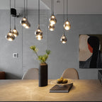 Smoke-toned glass pendants from Clérachic hang in a loose cluster above a stone table with a vase and a bowl of fruit.