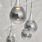 Close view of chrome-finish Clérachic pendants, their mirrored glass shades reflecting the room and a warm bulb inside each.