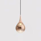 Rose gold Clérachic pendant with a polished teardrop shade, hanging from a black cord against a pale grey backdrop.