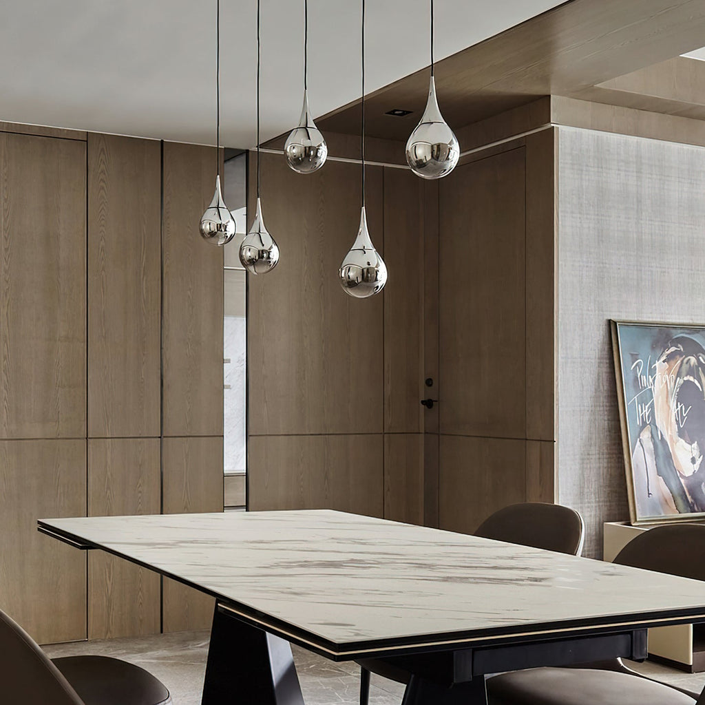 Chrome-finish Clérachic pendants hang at different heights over a marble-topped dining table in a timber-panelled room.