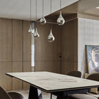 Chrome-finish Clérachic pendants hang at different heights over a marble-topped dining table in a timber-panelled room.