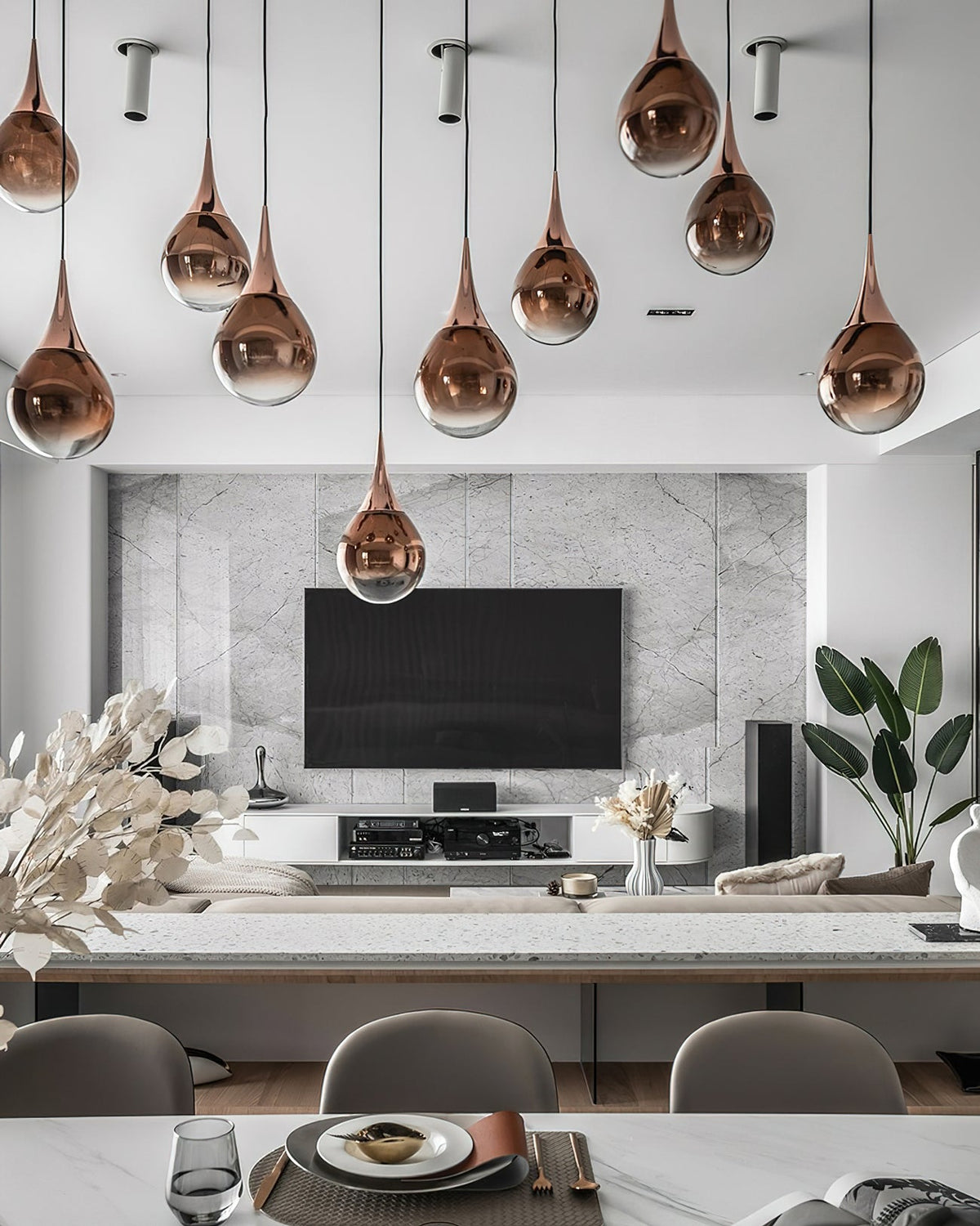 Rose gold glass Clérachic pendants in a mixed-height cluster above a dining table, with a wall-mounted television behind.