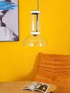 Clear glass cylinder and shallow dome from Clérachic against a bright yellow wall, beside an orange sofa and an open magazine.