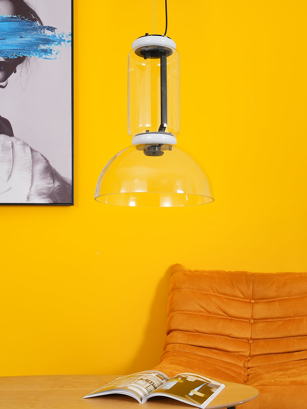 Closer view of this Clérachic pendant's glass cylinder and dome in front of a yellow wall, with an orange sofa below.