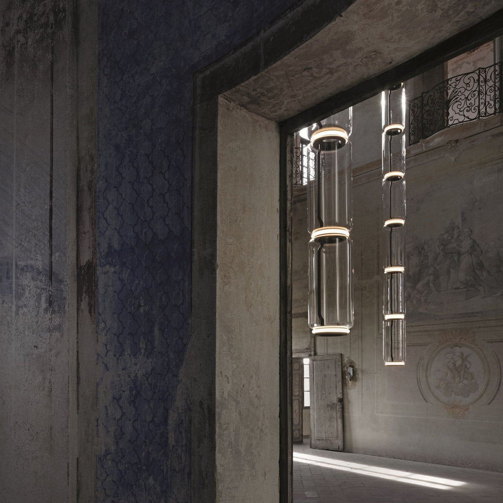 Two columns of stacked glass cylinders hang beyond a stone doorway, Clérachic pendants in an old room with painted plaster walls.