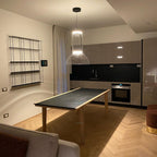 Clérachic pendant with a glass cylinder and dome above a dark-topped table, with a modern kitchen and herringbone floor behind.
