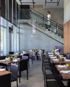 Single stacked-cylinder Clérachic pendant hanging beside a stone-clad staircase above a restaurant with laid tables.