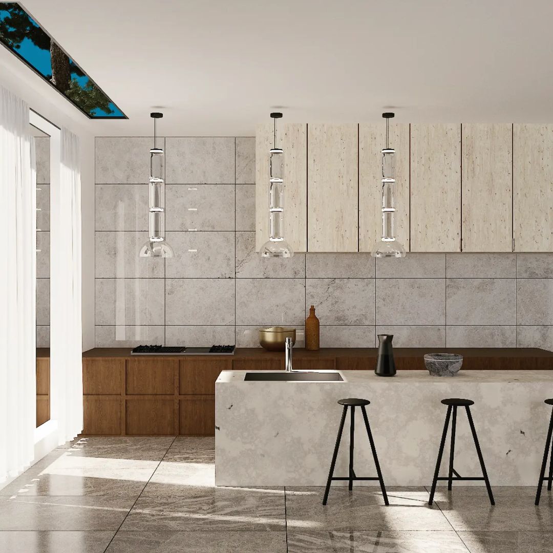 Three slim stacked-glass Clérachic pendants hang above a stone kitchen island with black stools and walnut cabinets.