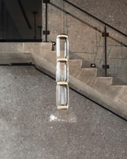 Stacked glass cylinders over a cone, this Clérachic pendant lit beside a stone staircase with a glass balustrade.