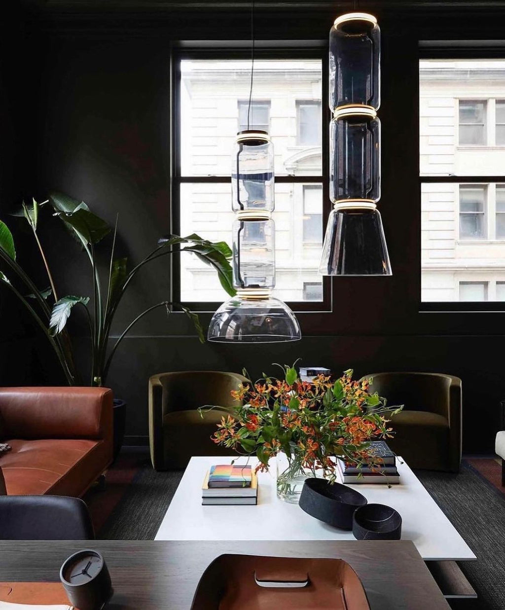 Stacked glass cylinders and a dome from Clérachic hang in a dark lounge with a leather sofa and a flower arrangement.